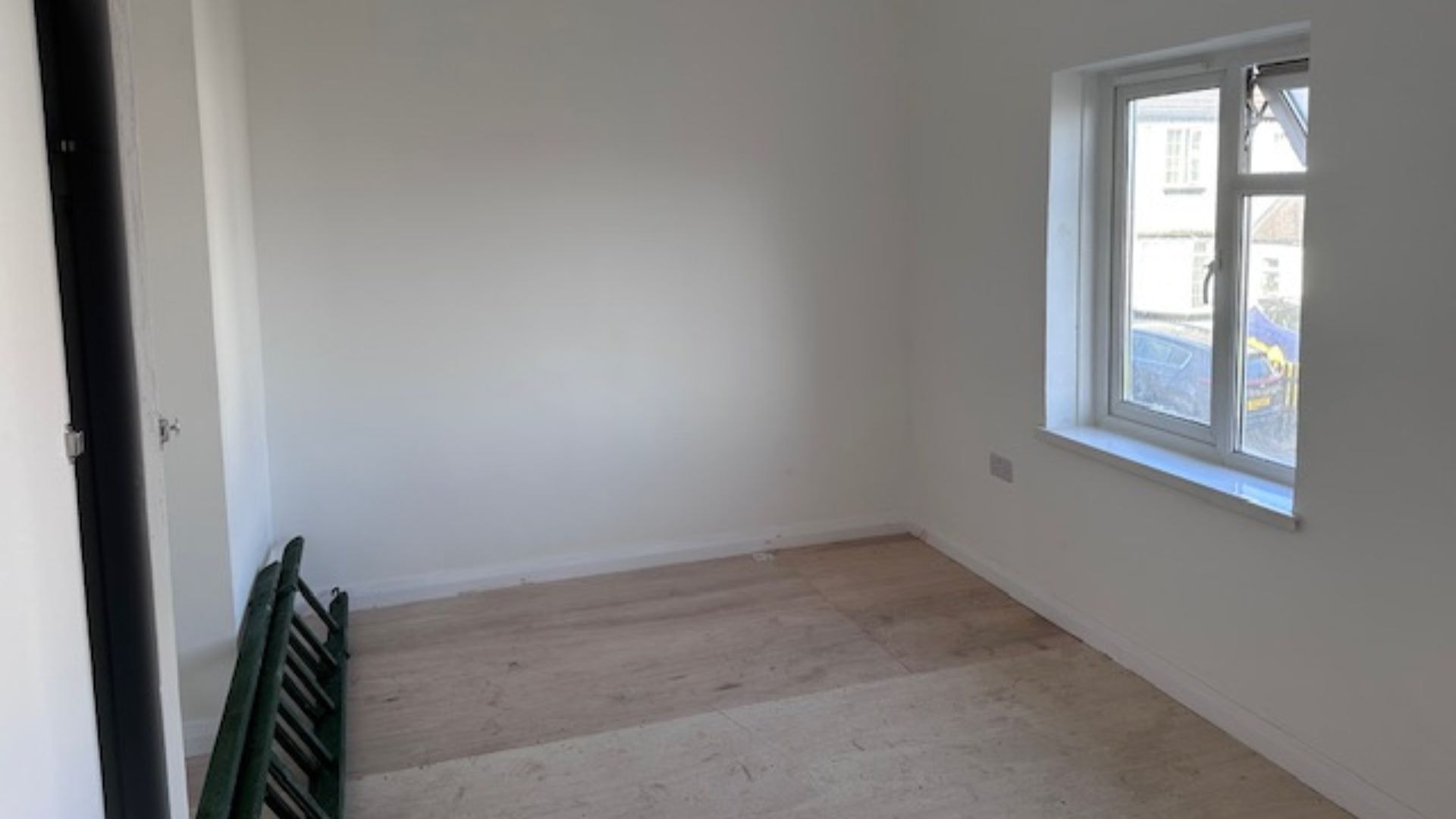 Empty room with white walls, wooden flooring, and a window letting in natural light.